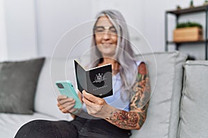 Middle age grey-haired woman using smartphone holding australia passport at home