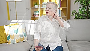 Middle age grey-haired woman using smartphone suffering for cervical pain at home