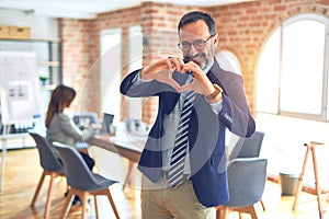 Middle age handsome businessman wearing glasses   standing at the office smiling in love showing heart symbol and shape with hands