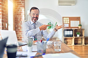 Middle age handsome businessman wearing tie sitting using laptop at the office amazed and smiling to the camera while presenting