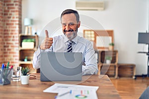 Middle age handsome businessman wearing tie sitting using laptop at the office doing happy thumbs up gesture with hand