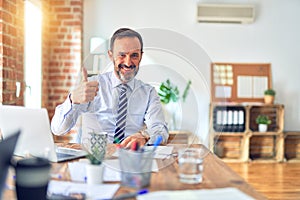 Middle age handsome businessman wearing tie sitting using laptop at the office doing happy thumbs up gesture with hand