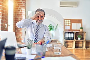 Middle age handsome businessman wearing tie sitting using laptop at the office doing ok gesture with hand smiling, eye looking