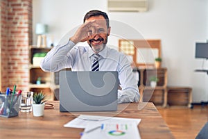 Middle age handsome businessman wearing tie sitting using laptop at the office doing ok gesture with hand smiling, eye looking