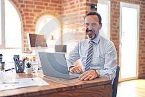 Middle age handsome businessman wearing tie sitting using laptop at the office with a happy and cool smile on face