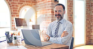 Middle age handsome businessman wearing tie sitting using laptop at the office happy face smiling with crossed arms looking at the