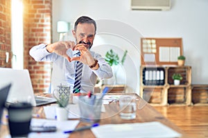 Middle age handsome businessman wearing tie sitting using laptop at the office smiling in love showing heart symbol and shape with