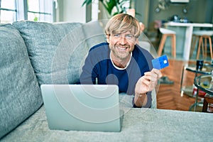 Middle age handsome caucasian man relaxing at home doing online shopping using credit card on computer laptop