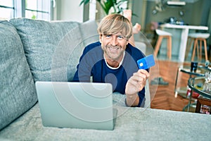 Middle age handsome caucasian man relaxing at home doing online shopping using credit card on computer laptop