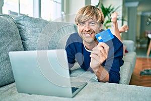 Middle age handsome caucasian man relaxing at home doing online shopping using credit card on computer laptop