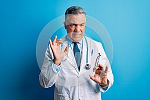 Middle age handsome grey-haired doctor man wearing coat and blue stethoscope disgusted expression, displeased and fearful doing