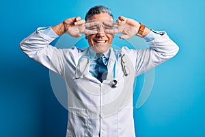 Middle age handsome grey-haired doctor man wearing coat and blue stethoscope Doing peace symbol with fingers over face, smiling