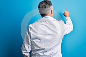 Middle age handsome grey-haired doctor man wearing coat and blue stethoscope Posing backwards pointing ahead with finger hand