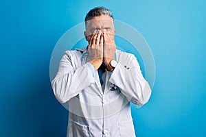 Middle age handsome grey-haired doctor man wearing coat and blue stethoscope rubbing eyes for fatigue and headache, sleepy and