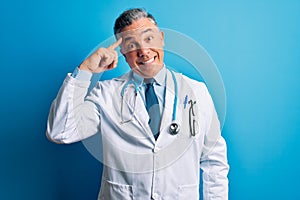 Middle age handsome grey-haired doctor man wearing coat and blue stethoscope Smiling pointing to head with one finger, great idea