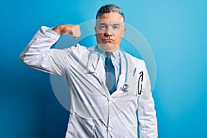 Middle age handsome grey-haired doctor man wearing coat and blue stethoscope Strong person showing arm muscle, confident and proud