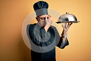 Middle age handsome grey-haired waiter man wearing cooker uniform and hat holding tray tired rubbing nose and eyes feeling fatigue