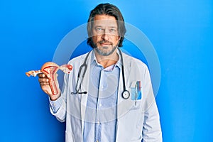 Middle age handsome gynecologist man holding anatomical model of female genital organ thinking attitude and sober expression