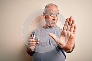 Middle age handsome hoary man drinking glass of water over isolated white background with open hand doing stop sign with serious