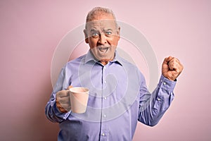 Middle age handsome hoary man drinking mug of coffee over isolated pink background screaming proud and celebrating victory and