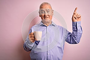 Middle age handsome hoary man drinking mug of coffee over isolated pink background surprised with an idea or question pointing