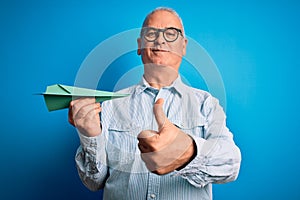 Middle age handsome hoary man holding paper airplane over isolated blue background happy with big smile doing ok sign, thumb up