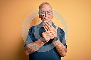 Middle age handsome hoary man wearing casual polo and glasses over yellow background Suffering pain on hands and fingers,