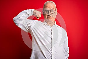 Middle age handsome hoary man wearing casual shirt and glasses over red background Strong person showing arm muscle, confident and