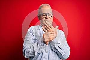 Middle age handsome hoary man wearing casual striped shirt and glasses over red background Suffering pain on hands and fingers,