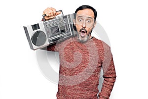 Middle age handsome man listening vintage boombox over isolated white background scared and amazed with open mouth for surprise,
