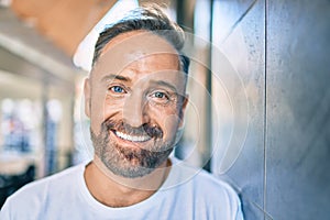 Middle age handsome man smiling happy leaning on the wall at the city