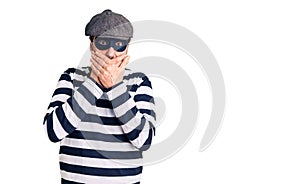 Middle age handsome man wearing burglar mask shocked covering mouth with hands for mistake