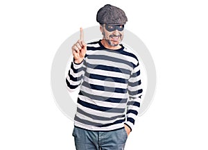 Middle age handsome man wearing burglar mask showing and pointing up with finger number one while smiling confident and happy