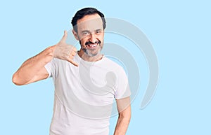 Middle age handsome man wearing casual t-shirt smiling doing phone gesture with hand and fingers like talking on the telephone