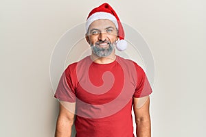 Middle age handsome man wearing christmas hat and summer t-shirt with a happy and cool smile on face