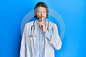 Middle age handsome man wearing doctor uniform and stethoscope asking to be quiet with finger on lips