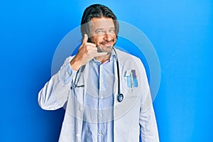 Middle age handsome man wearing doctor uniform and stethoscope smiling doing phone gesture with hand and fingers like talking on