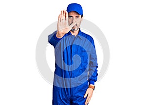 Middle age handsome man wearing mechanic uniform doing stop sing with palm of the hand