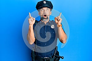 Middle age handsome man wearing police uniform amazed and surprised looking up and pointing with fingers and raised arms