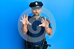 Middle age handsome man wearing police uniform smiling funny doing claw gesture as cat, aggressive and sexy expression