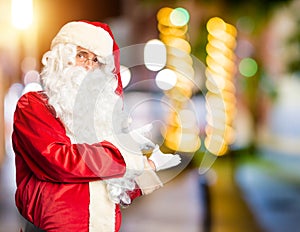 Middle age handsome man wearing Santa Claus costume and beard standing Inviting to enter smiling natural with open hand