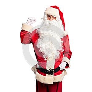 Middle age handsome man wearing Santa Claus costume and beard standing Strong person showing arm muscle, confident and proud of