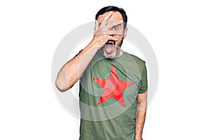 Middle age handsome man wearing t-shirt with revolutionary red star over white background peeking in shock covering face and eyes