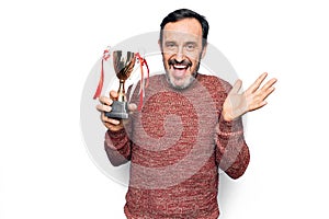 Middle age handsome man winning trophy for victory over isolated white background celebrating achievement with happy smile and