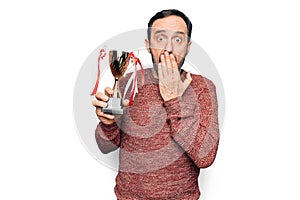 Middle age handsome man winning trophy for victory over isolated white background covering mouth with hand, shocked and afraid for