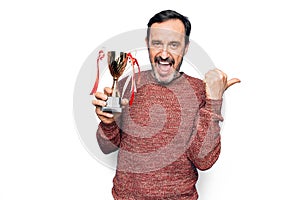 Middle age handsome man winning trophy for victory over isolated white background pointing thumb up to the side smiling happy with