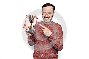 Middle age handsome man winning trophy for victory over isolated white background smiling happy pointing with hand and finger