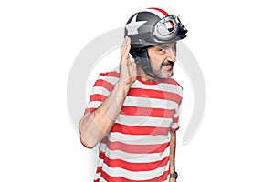 Middle age handsome motorcyclist man wearing moto helmet over isolated white background smiling with hand over ear listening and