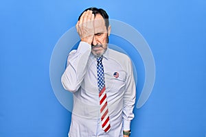 Middle age handsome patriotic businessman wearing united states tie over blue background surprised with hand on head for mistake,