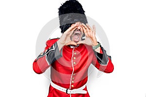 Middle age handsome wales guard man wearing traditional uniform over white background Shouting angry out loud with hands over